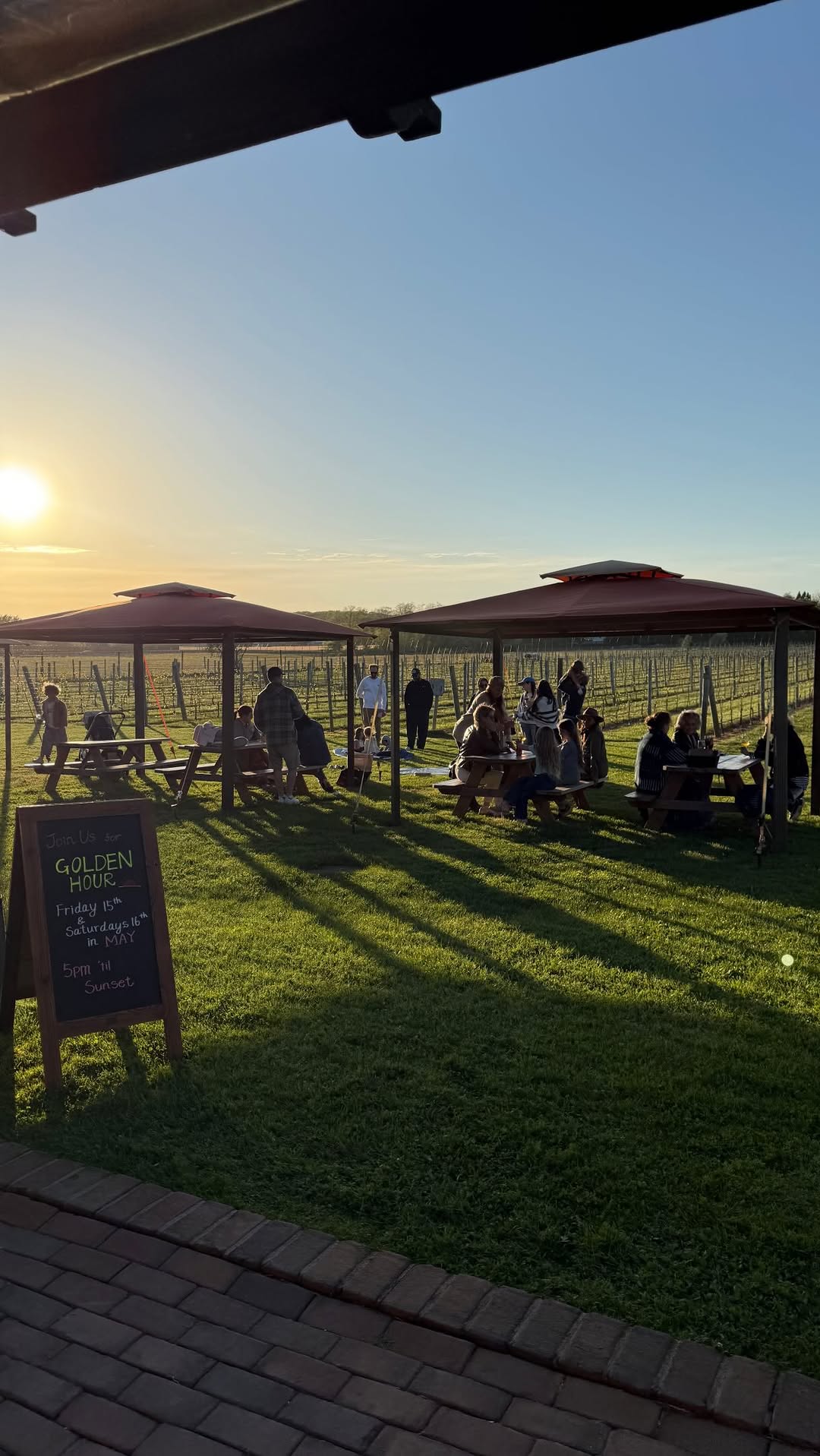 Golden hour at the vineyard — picnic tables under gazebos and a chalkboard reading Golden Hour, 5pm til sunset
