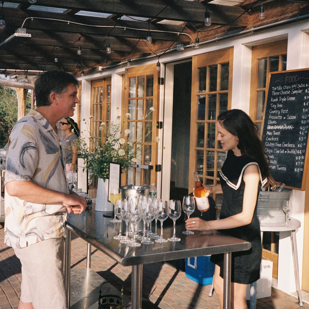 A pour of rosé at the tasting bar under the pergola, chalkboard food menu behind
